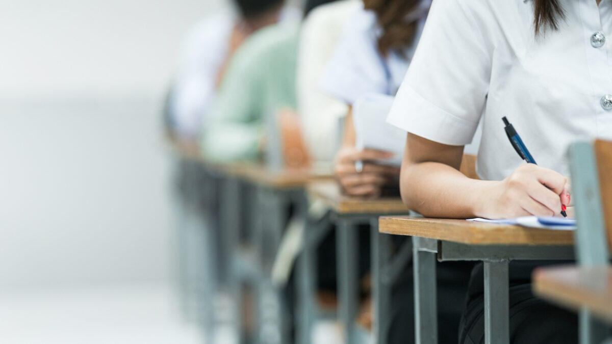 Students Taking Exam in Classroom Setting. Students in uniforms are seated in a classroom, writing answers during an exam, highlighting focus and academic testing.