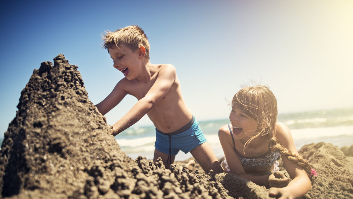 Happy kids are building sandcastle on a beach on a sunny summer day. Andalusia, Spain.