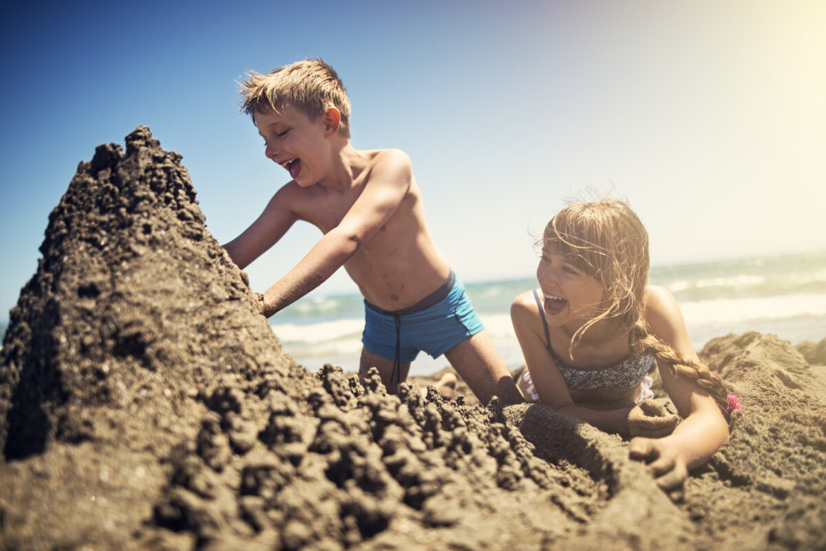 Happy kids are building sandcastle on a beach on a sunny summer day. Andalusia, Spain.