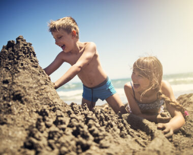 Happy kids are building sandcastle on a beach on a sunny summer day. Andalusia, Spain.