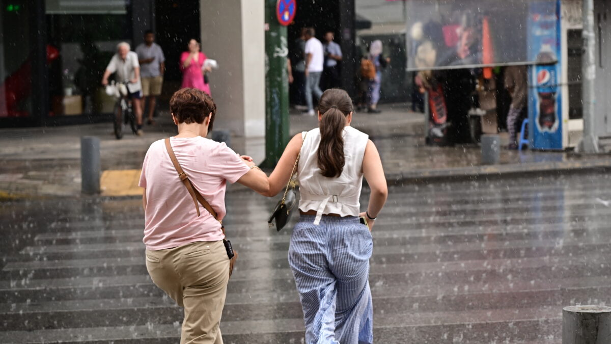 Δυο γυναίκες τρέχουν να προστατευτούν από τη βροχή