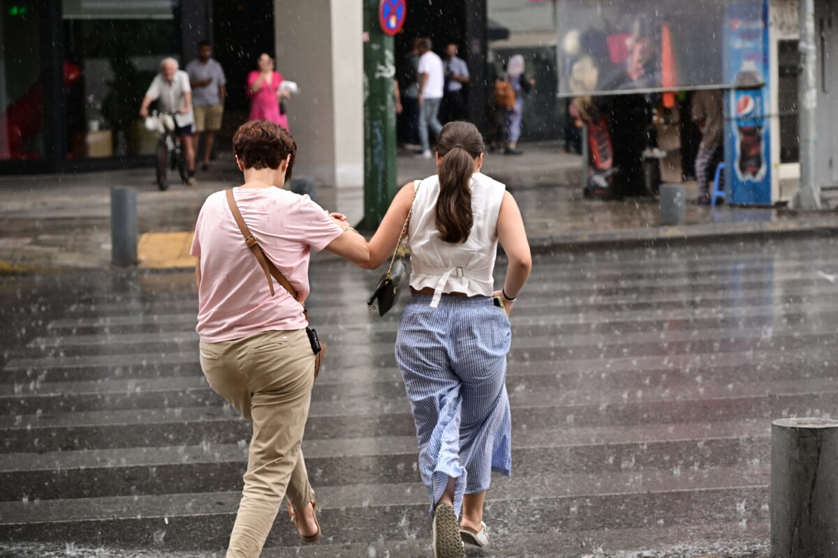 Δυο γυναίκες τρέχουν να προστατευτούν από τη βροχή