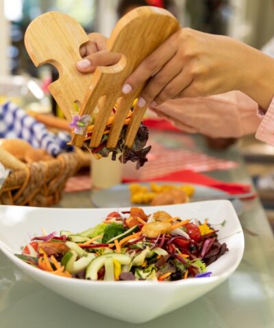 Side view mid section of a biracial woman using salad tongs to serve herself from a bowl of salad, sitting at a table during a family meal