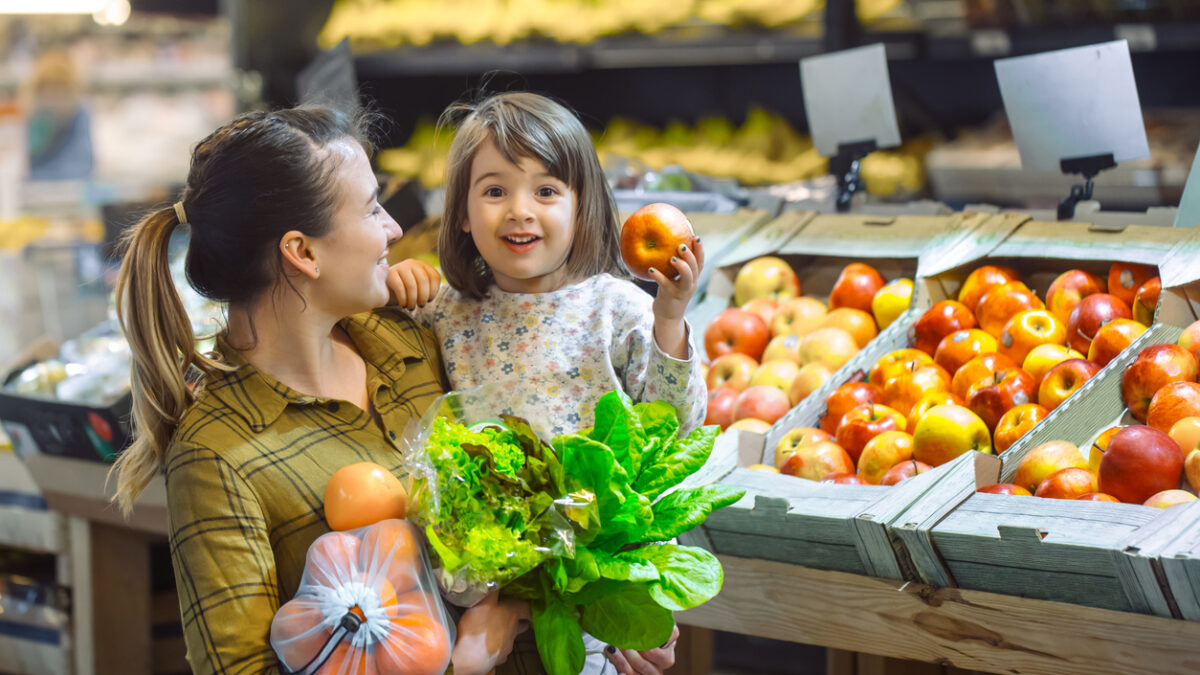 Family in the supermarket. Beautiful young mom and her little daughter smiling and buying food. The concept of healthy eating. Harvest