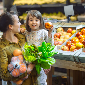 Family in the supermarket. Beautiful young mom and her little daughter smiling and buying food. The concept of healthy eating. Harvest