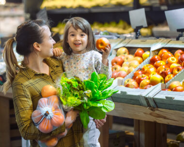Family in the supermarket. Beautiful young mom and her little daughter smiling and buying food. The concept of healthy eating. Harvest