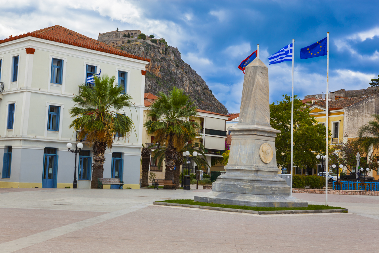 Beautiful Greek town of Nafplio (Nauplia), flags, obelisk and at the top the Ruins of fortress of Palamidi, Peloponnese, Greece.