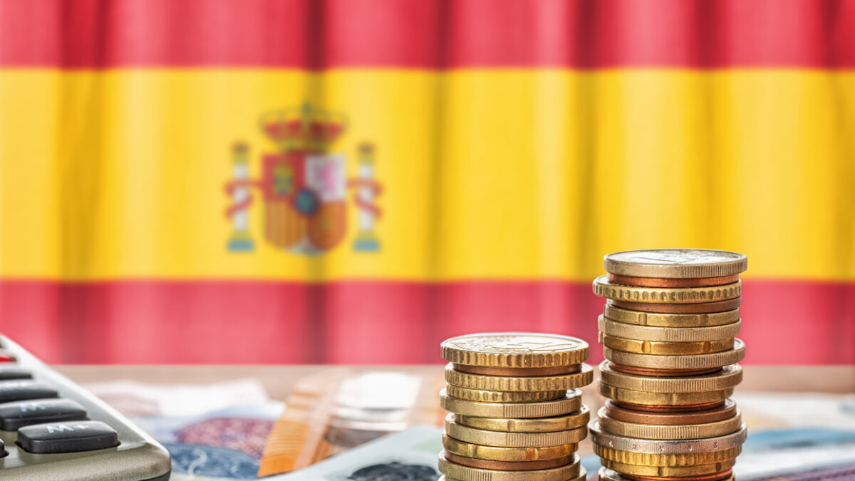 Euro banknotes and coins in front of the national flag of Spain