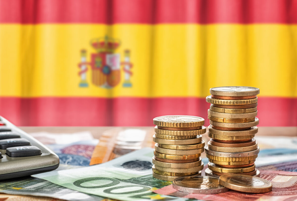 Euro banknotes and coins in front of the national flag of Spain