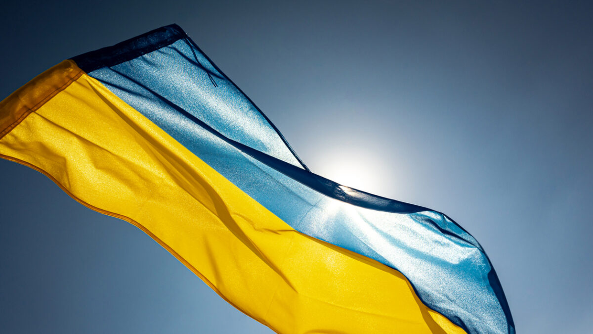 National flag of Ukraine waving outside on a wing facing the bright sky and the Sun