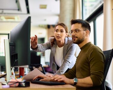 Young entrepreneur and his female coworker using desktop PC while working in the office.