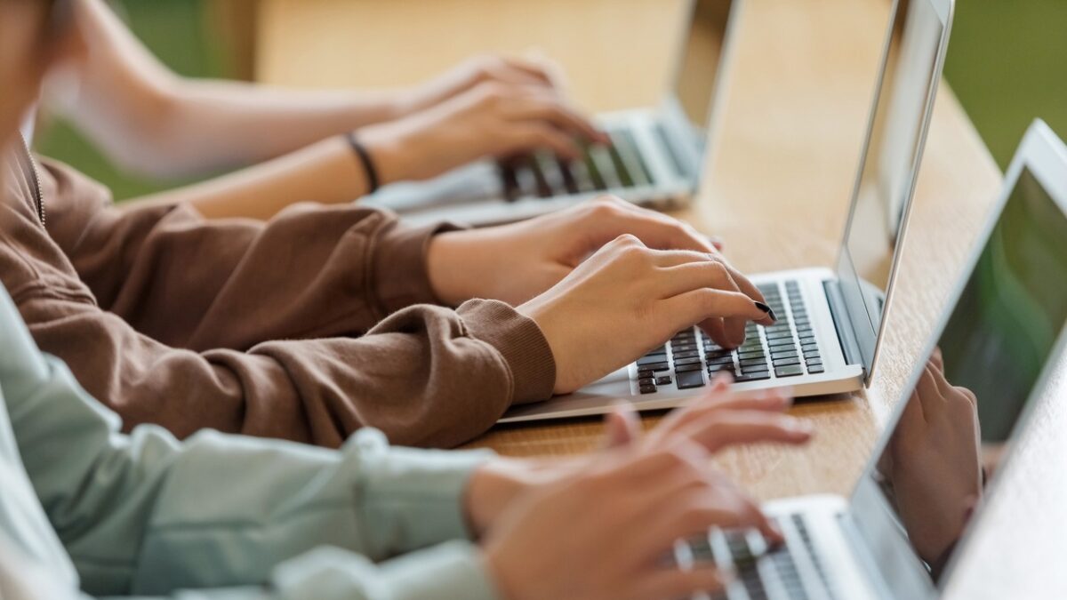 High school students sitting at the desk in the classroom during lesson, using laptops