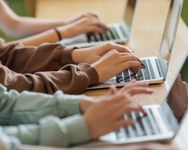 High school students sitting at the desk in the classroom during lesson, using laptops