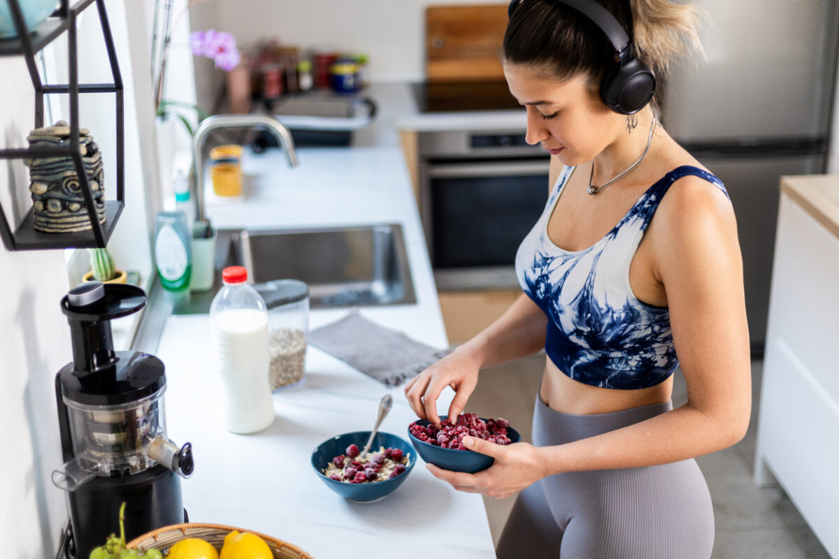 Athletic woman preparing and eating a healthy bowl of muesli with fruit standing in the kitchen at home