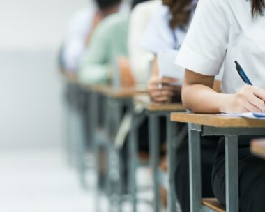 Students Taking Exam in Classroom Setting. Students in uniforms are seated in a classroom, writing answers during an exam, highlighting focus and academic testing