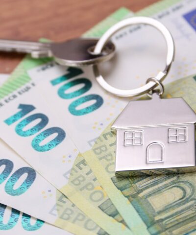 House key symbol pendant on one hundred euro banknotes, fanned out on a wooden desk