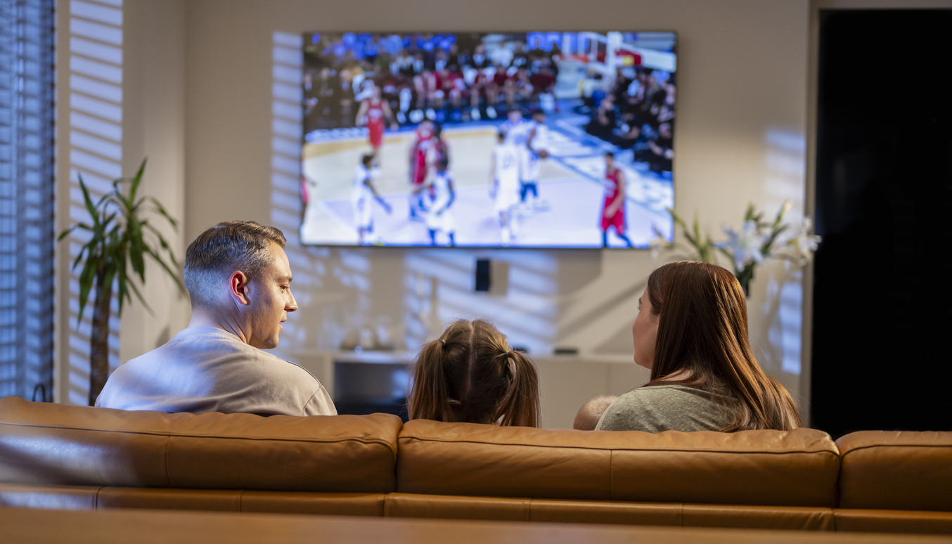 Overjoyed family, dad mom and children sport fans sitting on couch in living room at home watching basketball match on tv with favorite team, celebrating championship win. Rear view.