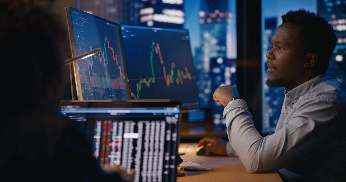 Financial advisors observe and analyze stock market charts, discussing prices, potential consequences, and developing investment strategies for the future. Modern office in skyscarper on high floor