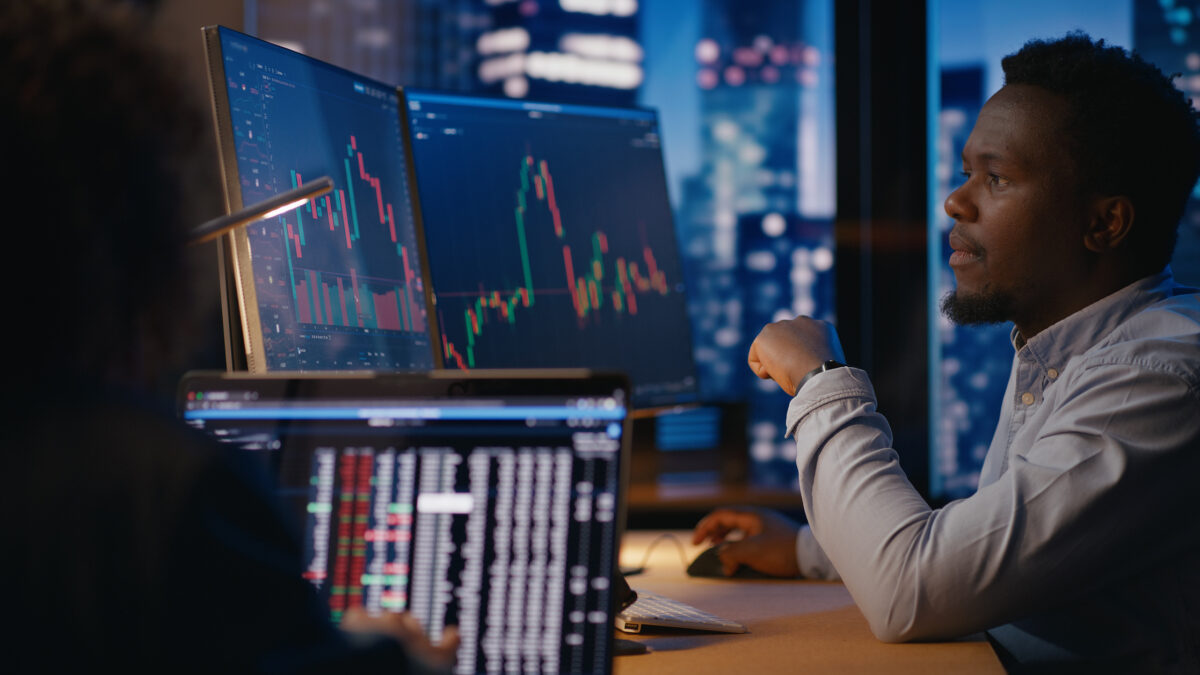 Financial advisors observe and analyze stock market charts, discussing prices, potential consequences, and developing investment strategies for the future. Modern office in skyscarper on high floor