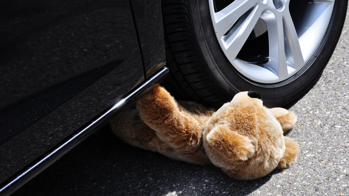 Teddy under car tires, symbolic car accident with playing children