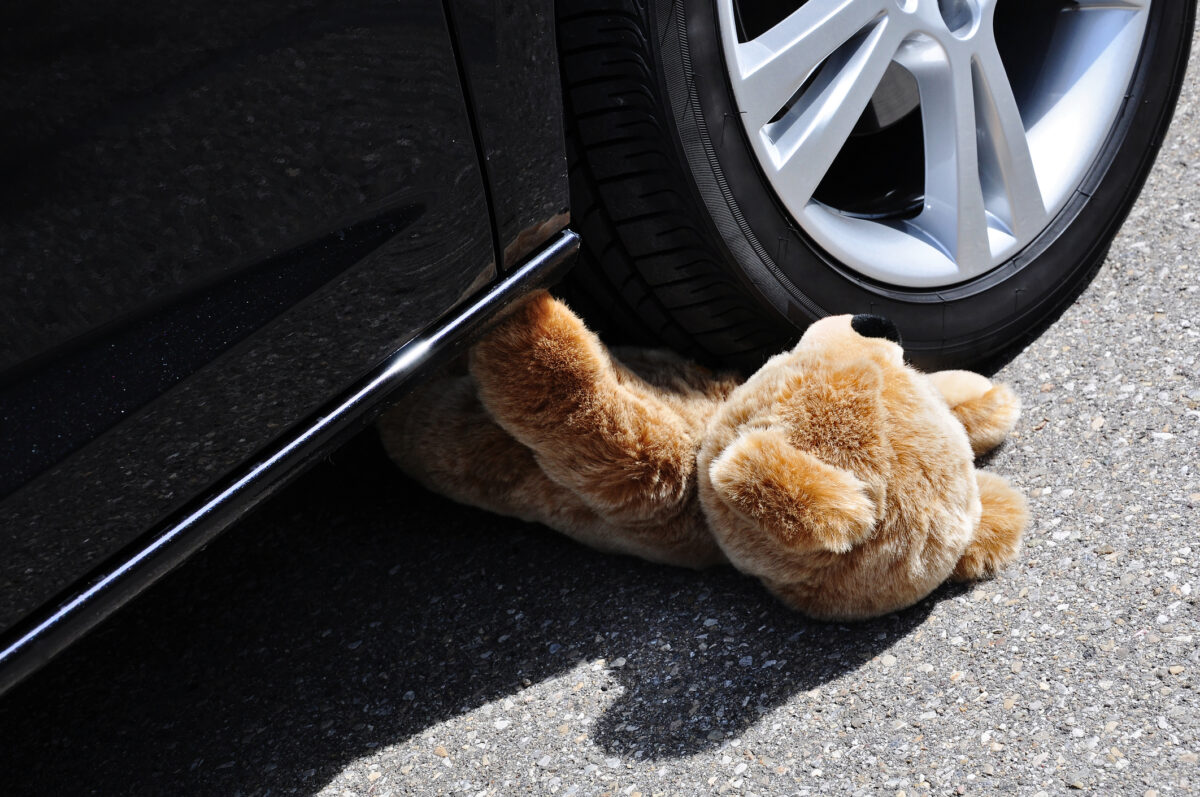 Teddy under car tires, symbolic car accident with playing children