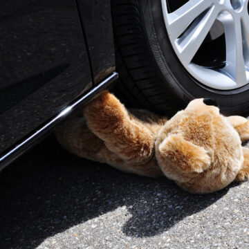 Teddy under car tires, symbolic car accident with playing children