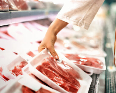 Closeup side view of unrecognizable woman chossing some fresh meat at local supermarket. The meat is cut into chops and packed into one pound packages. She has reached for a package of beef sirloin steaks