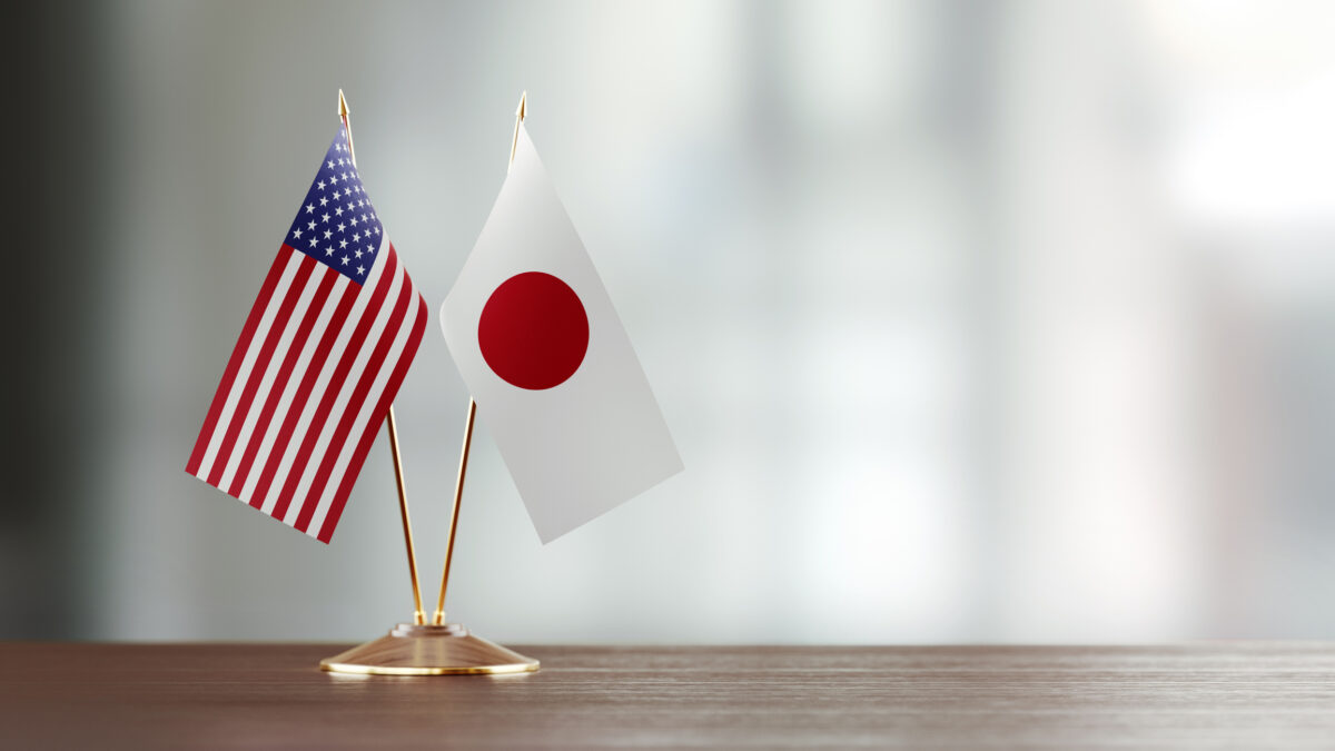 Japanese and American flag pair on desk over defocused background. Horizontal composition with copy space and selective focus