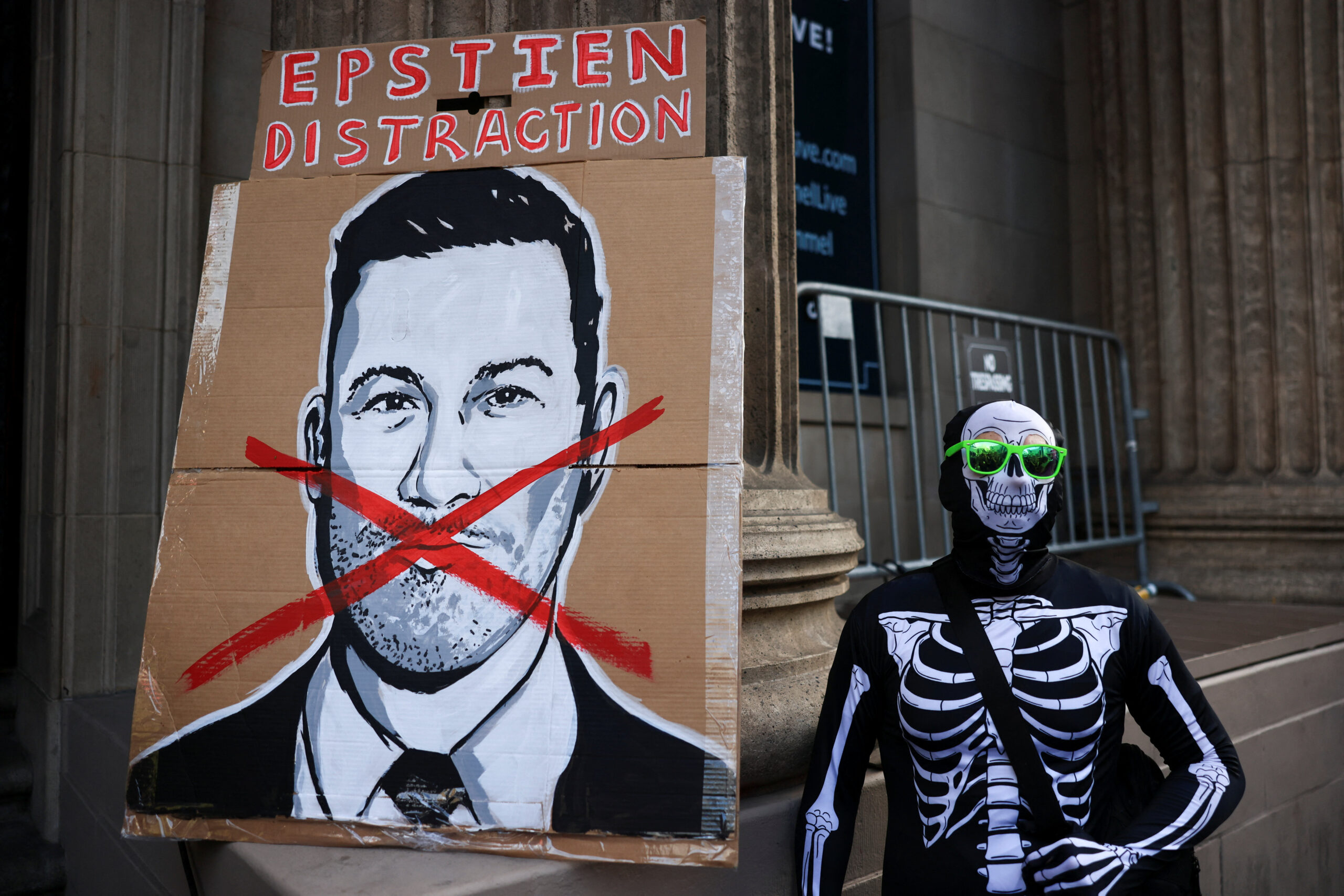 A protester dressed in a skeleton uniform stands next to a sign with Jimmy Kimmel