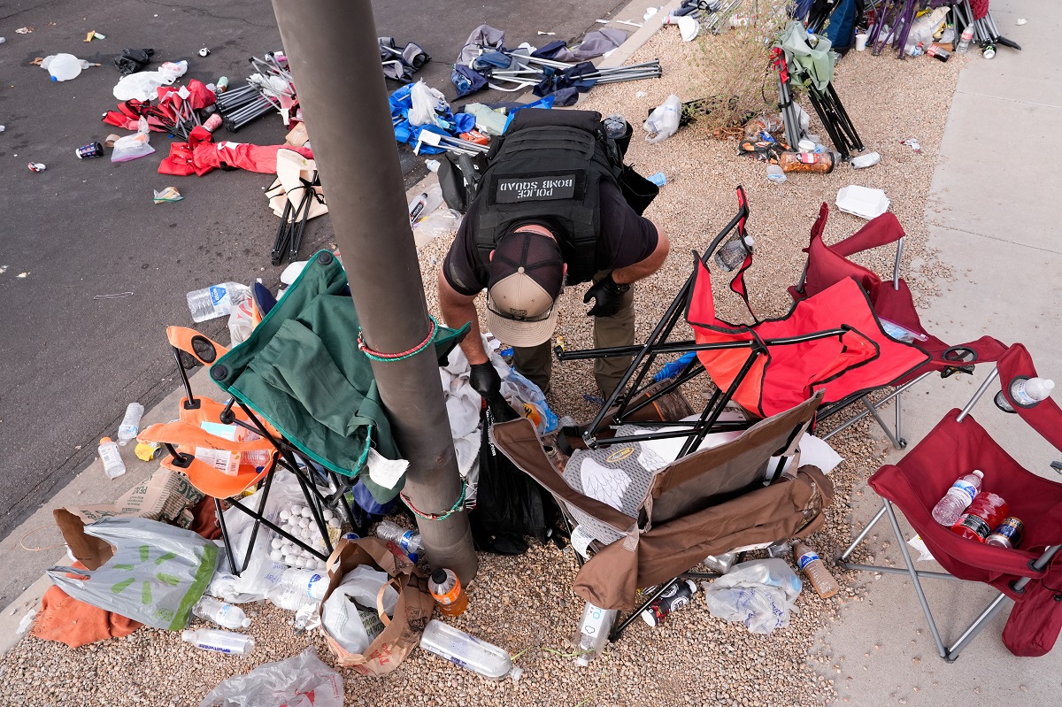 A police officer investigates trash and belongings left behind outside the venue by people who were waiting to attend a memorial service for slain conservative commentator Charlie Kirk, outside State Farm Stadium, in Glendale, Arizona, U.S., September 21, 2025.  REUTERS/Cheney Orr