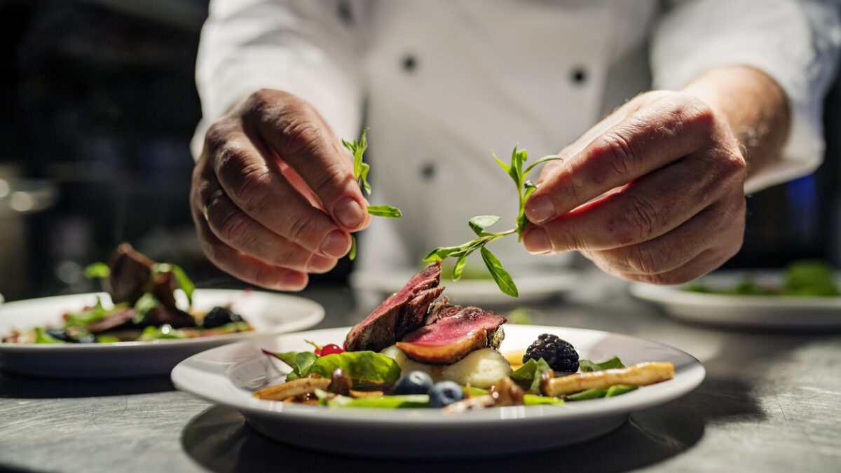 Chef adding the final flourish by adding some liquorice flavoured parsley to the dish. The dish is, pan fried pink duck breast onto a bed of parsnip puree with seasonal autumn vegetables and berries. Colour, horizontal with some copy space, photographed on location in a restaurant on the island of Møn in Denmark