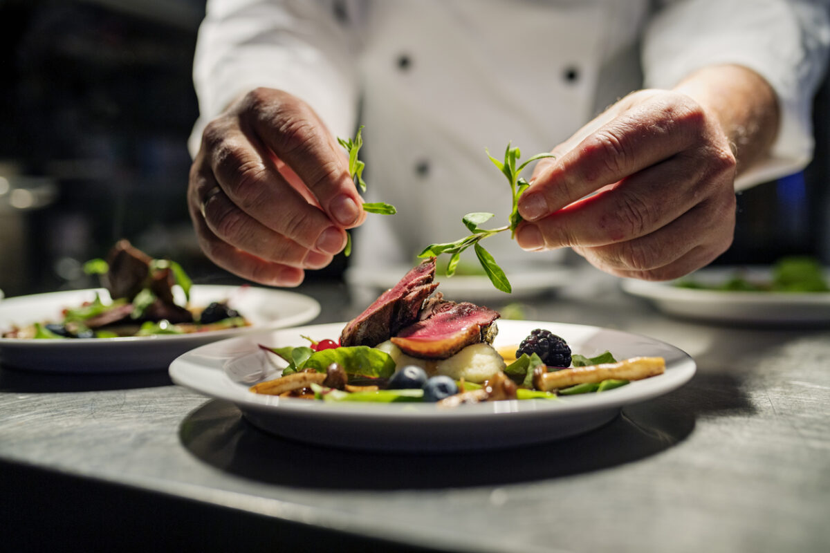 Chef adding the final flourish by adding some liquorice flavoured parsley to the dish. The dish is, pan fried pink duck breast onto a bed of parsnip puree with seasonal autumn vegetables and berries. Colour, horizontal with some copy space, photographed on location in a restaurant on the island of Møn in Denmark