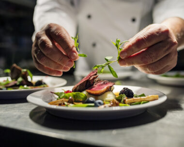 Chef adding the final flourish by adding some liquorice flavoured parsley to the dish. The dish is, pan fried pink duck breast onto a bed of parsnip puree with seasonal autumn vegetables and berries. Colour, horizontal with some copy space, photographed on location in a restaurant on the island of Møn in Denmark