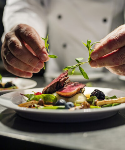 Chef adding the final flourish by adding some liquorice flavoured parsley to the dish. The dish is, pan fried pink duck breast onto a bed of parsnip puree with seasonal autumn vegetables and berries. Colour, horizontal with some copy space, photographed on location in a restaurant on the island of Møn in Denmark