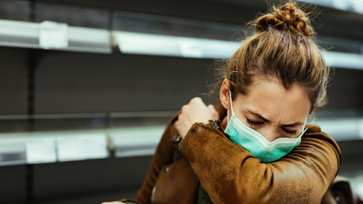 Sick woman buying in supermarket and coughing into elbow during COVID-19 pandemic.