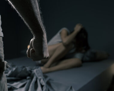 Man threatening a woman in the bedroom, she is scared and lying in bed, domestic violence concept