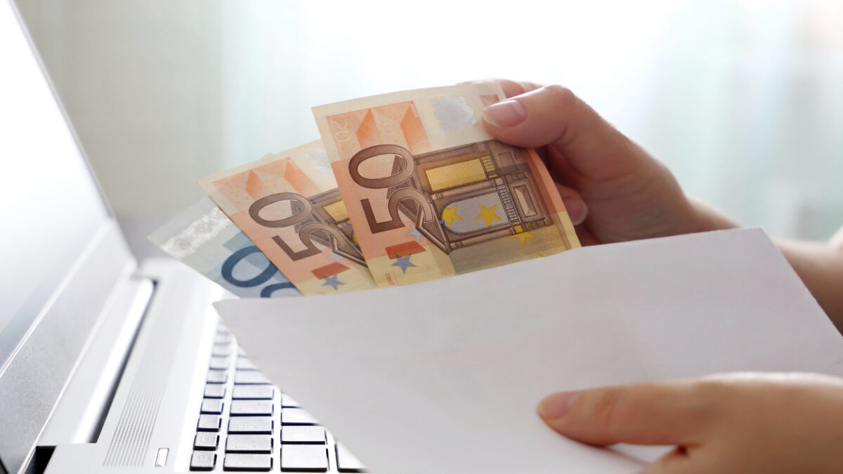 Woman pulls money out of an envelope on laptop background, wages, bonus or bribe concept