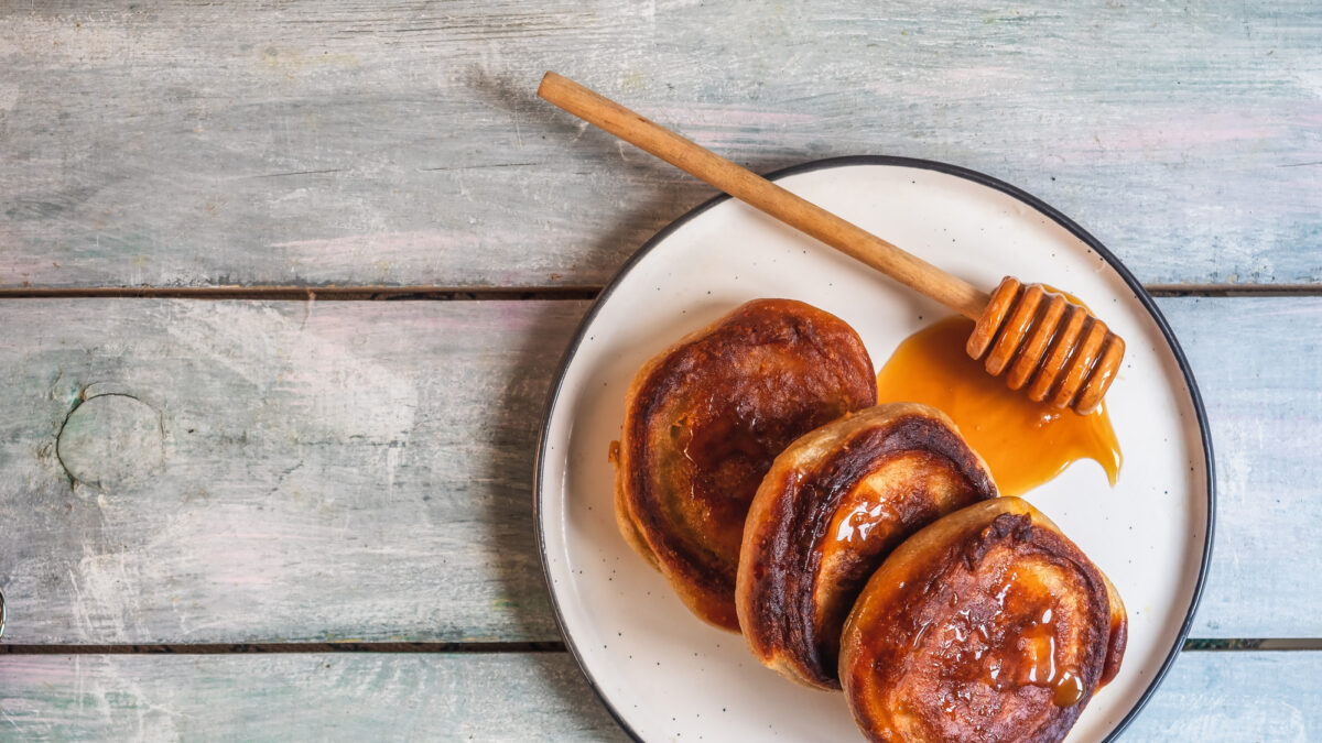Breakfast with pancakes and honey, wooden spoon on a light plate on the table top view close-up