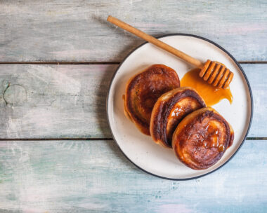 Breakfast with pancakes and honey, wooden spoon on a light plate on the table top view close-up