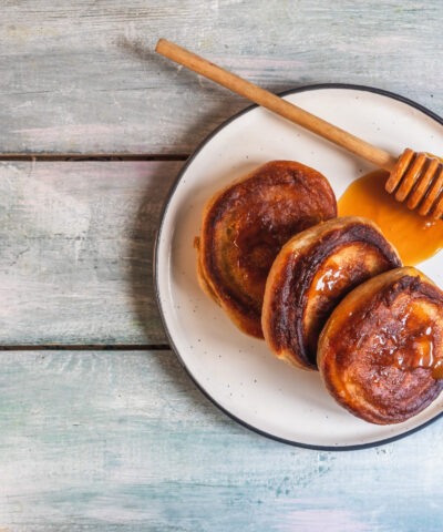 Breakfast with pancakes and honey, wooden spoon on a light plate on the table top view close-up