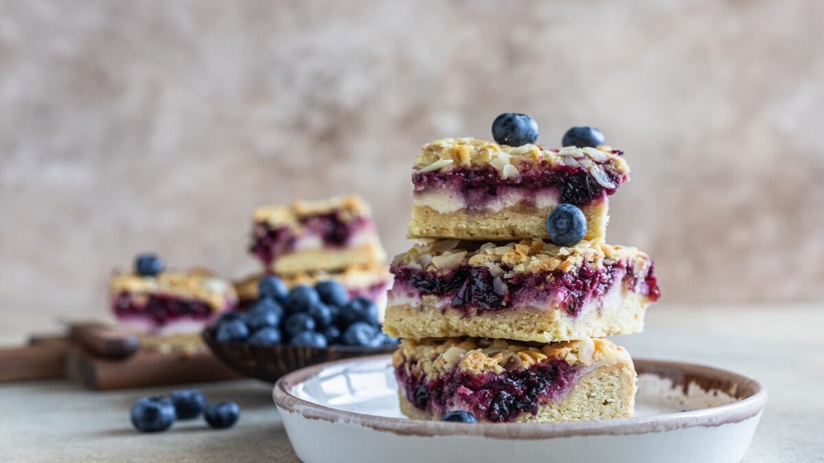 Crumble cheesecake bars with blueberry filling and fresh blueberries, concrete background. Bar slices with cheesecake, blueberry and streusel. Selective focus.