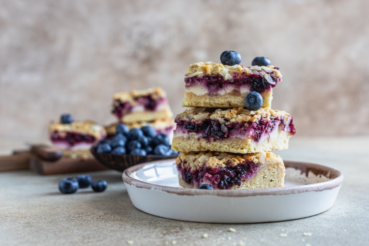 Crumble cheesecake bars with blueberry filling and fresh blueberries, concrete background. Bar slices with cheesecake, blueberry and streusel. Selective focus.