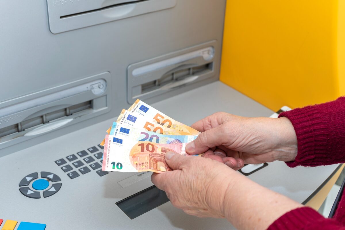 RETIRED SENIOR WOMAN WITHDRAWING MONEY FROM AN ATM. DIGITAL DIVIDE AMONG THE ELDERLY
