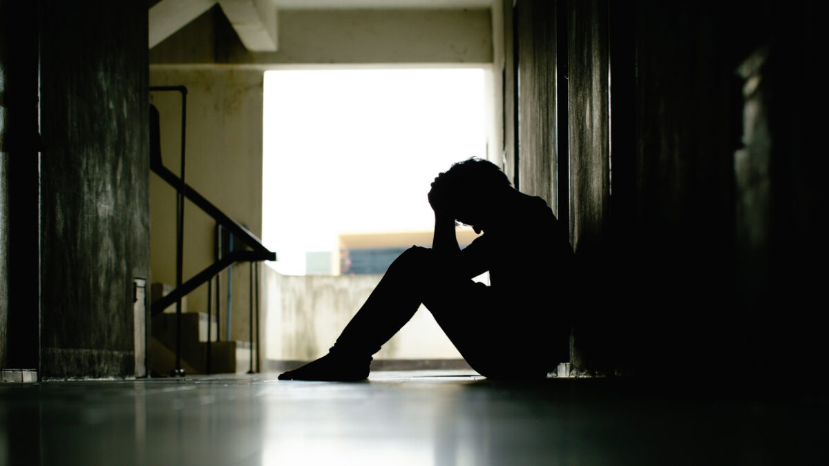 Silhouette of depressed man sitting head in hands on the walkway of residence building. Sad man, lonely and unhappy.Negative emotion and mental health concept. The impact of Economy crisis. dramatic.