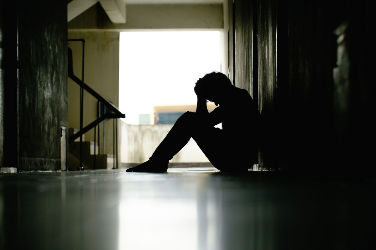 Silhouette of depressed man sitting head in hands on the walkway of residence building. Sad man, lonely and unhappy.Negative emotion and mental health concept. The impact of Economy crisis. dramatic.