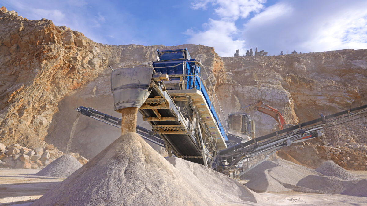Stone crushing machine at open pit mining and processing plant for crushed stone. Piles of gravel stone and conveyor belts on the side of the road. Concepts of industry and building materials, sand and gravel