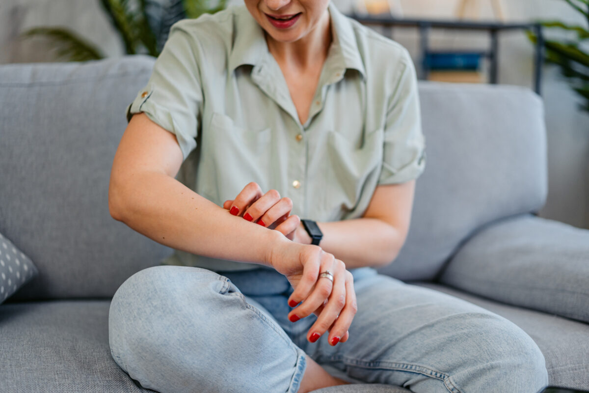 Mid-adult woman having a rash (skin condition) while sitting on the sofa at home.
