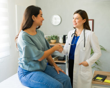 Female doctor happily shaking hands with her hispanic patient after a successful consultation in her office