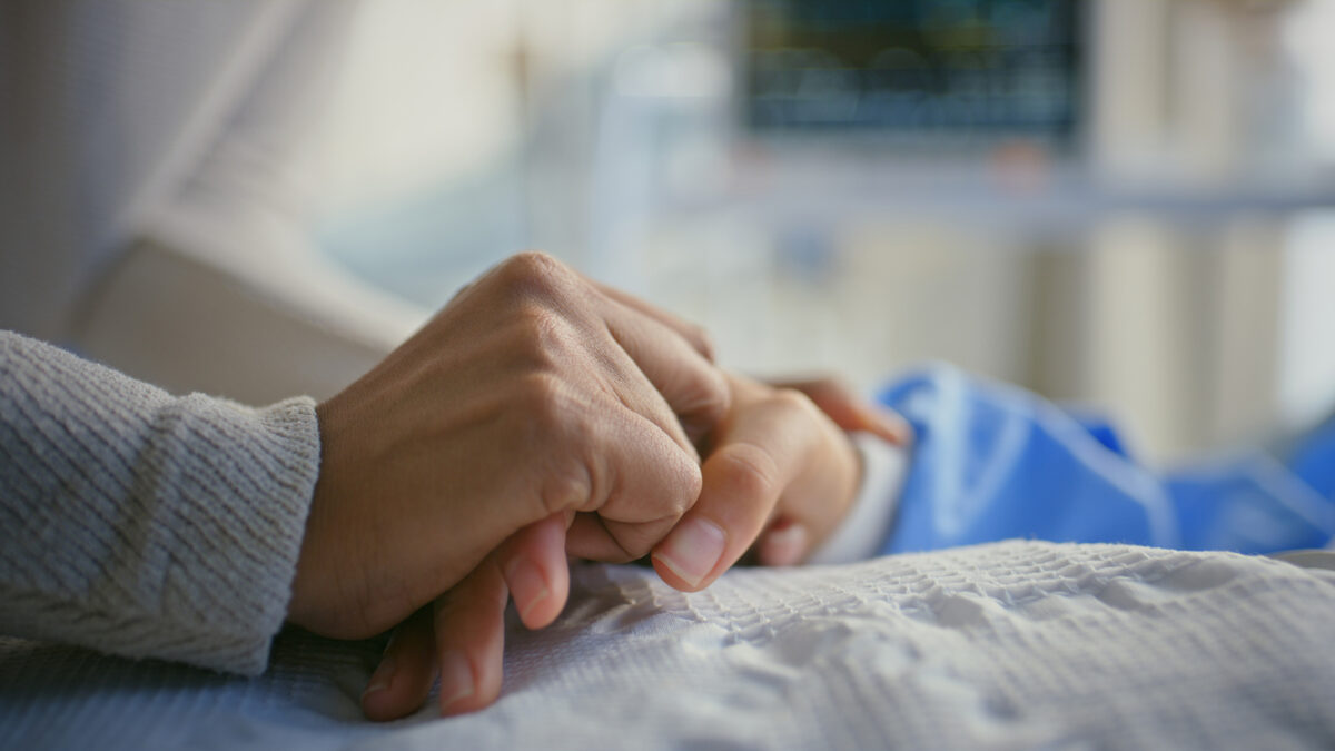 Holding hands, patient and person by hospital bed for support, sick and empathy for wellness. People, care and console for health with connection, love and help with comfort for recovery at clinic