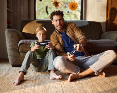 Carefree single father and his son having fun while playing video games on TV in the living room.